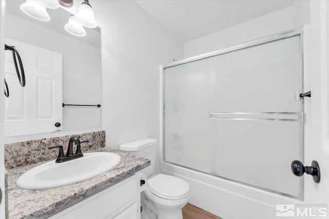 full bath featuring toilet, bath / shower combo with glass door, and vanity