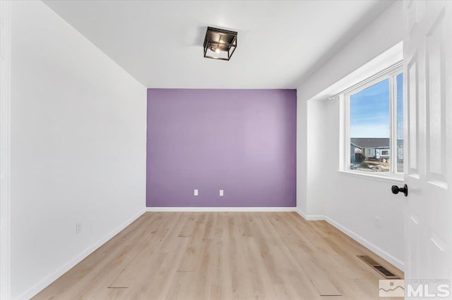 spare room featuring light wood finished floors, visible vents, and baseboards