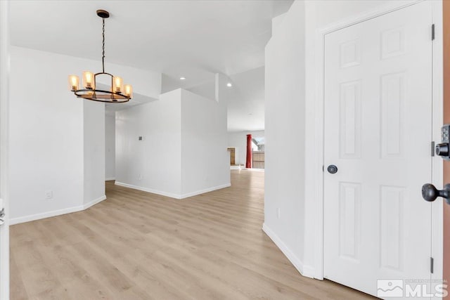 empty room with a notable chandelier, light wood-style flooring, and baseboards