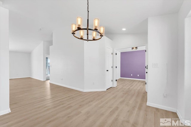 empty room with a chandelier, vaulted ceiling, light wood-type flooring, and baseboards