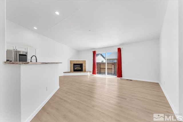 unfurnished living room with light wood finished floors, lofted ceiling, recessed lighting, a tiled fireplace, and baseboards