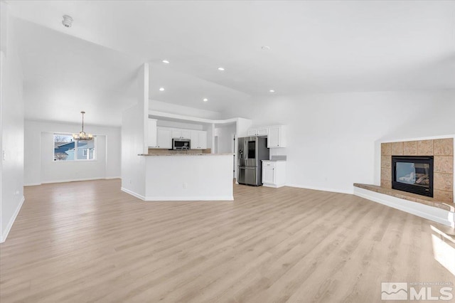 unfurnished living room with light wood-style floors, baseboards, vaulted ceiling, and a tiled fireplace