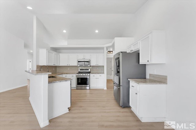 kitchen with tasteful backsplash, white cabinets, appliances with stainless steel finishes, a peninsula, and a sink