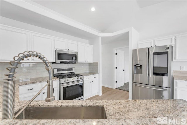 kitchen featuring white cabinetry, appliances with stainless steel finishes, backsplash, light stone countertops, and light wood finished floors