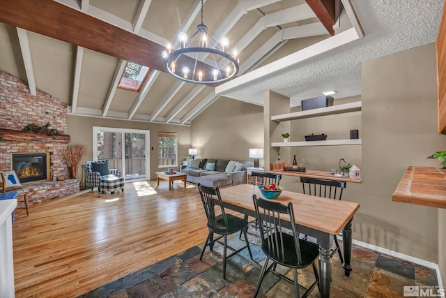 dining room with a notable chandelier, a fireplace, a textured ceiling, wood finished floors, and beamed ceiling