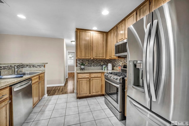 kitchen with brown cabinets, backsplash, appliances with stainless steel finishes, light tile patterned flooring, and a sink