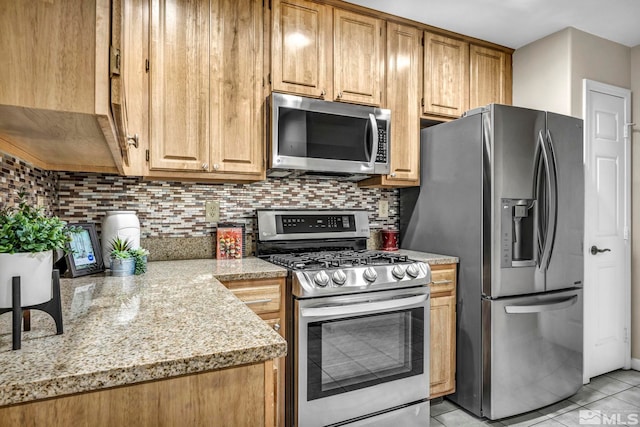 kitchen featuring appliances with stainless steel finishes, light tile patterned floors, light stone counters, and tasteful backsplash