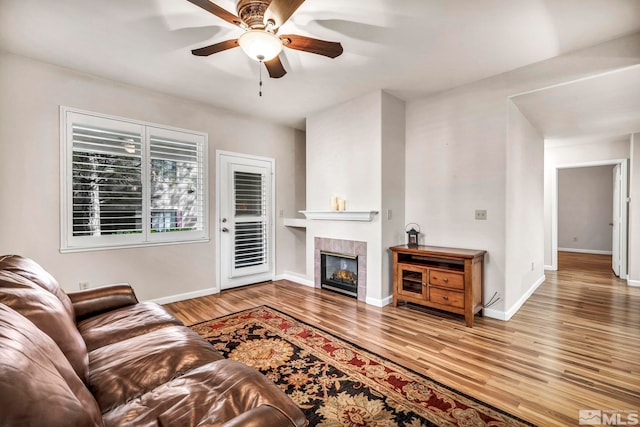 living room featuring ceiling fan, baseboards, a tiled fireplace, and wood finished floors