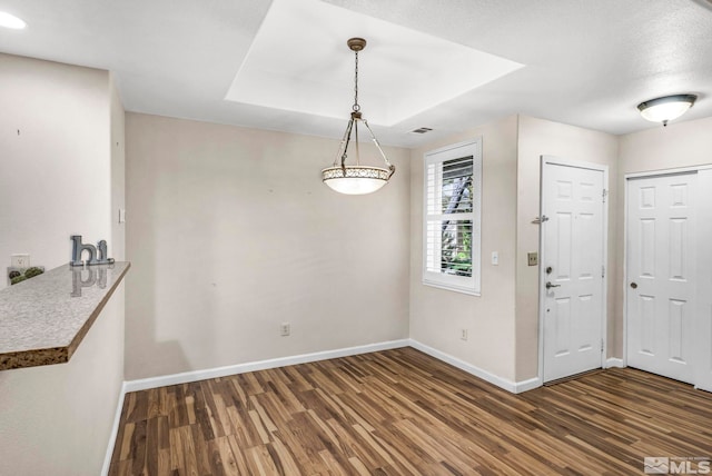 entryway with a raised ceiling, visible vents, baseboards, and wood finished floors