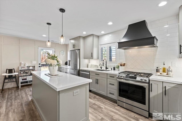 kitchen featuring wall chimney exhaust hood, appliances with stainless steel finishes, a center island, gray cabinets, and a sink