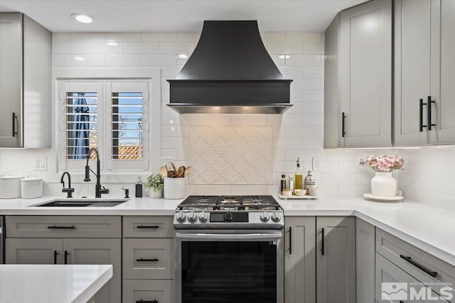 kitchen featuring stainless steel gas range, custom range hood, a sink, and gray cabinetry