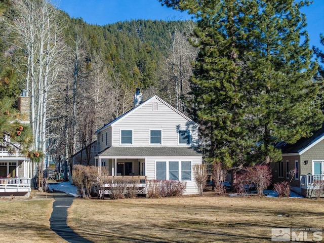 traditional home featuring a front yard, covered porch, and a view of trees