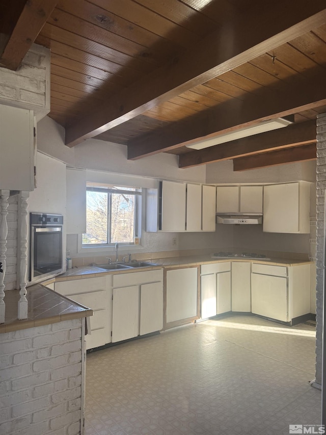 kitchen featuring tile countertops, wooden ceiling, oven, light floors, and a sink