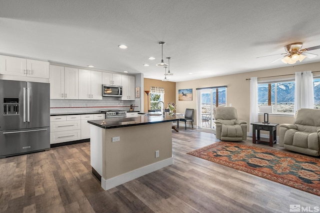 kitchen featuring tasteful backsplash, dark countertops, appliances with stainless steel finishes, open floor plan, and a sink