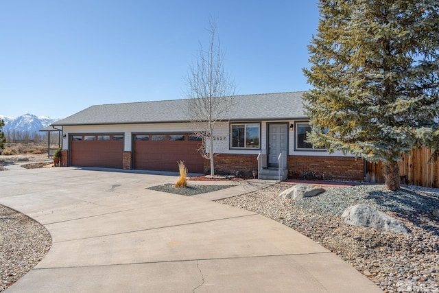 ranch-style house featuring a mountain view, a garage, brick siding, fence, and driveway