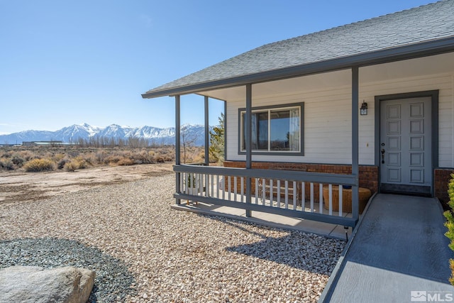 entrance to property featuring covered porch, a shingled roof, brick siding, and a mountain view