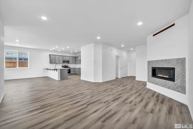 unfurnished living room with light wood-style flooring, a fireplace, baseboards, and recessed lighting