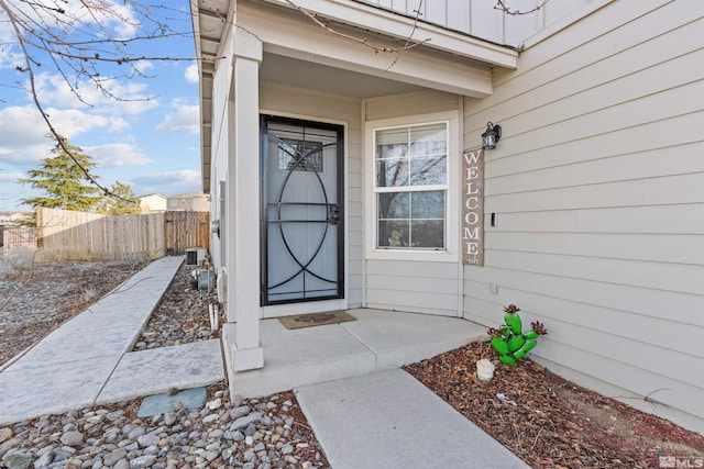 view of exterior entry featuring board and batten siding, cooling unit, and fence