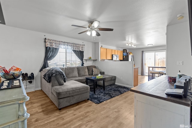 living area with baseboards, a healthy amount of sunlight, a ceiling fan, and light wood-style floors