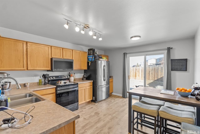 kitchen featuring light countertops, appliances with stainless steel finishes, light brown cabinets, a sink, and light wood-type flooring