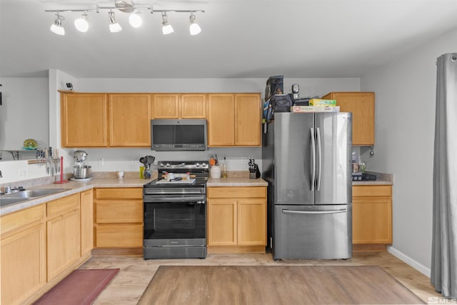 kitchen with appliances with stainless steel finishes, light countertops, a sink, and light wood-style flooring