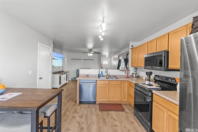 kitchen featuring a peninsula, a sink, light countertops, appliances with stainless steel finishes, and light wood-type flooring