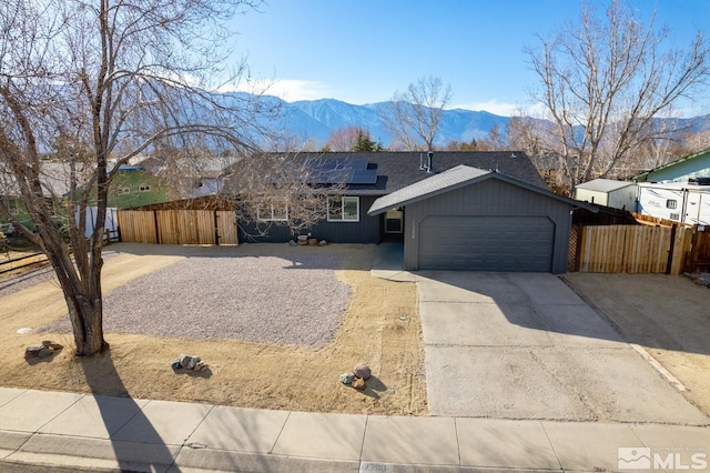 view of front of house featuring a garage, fence, a mountain view, and roof mounted solar panels