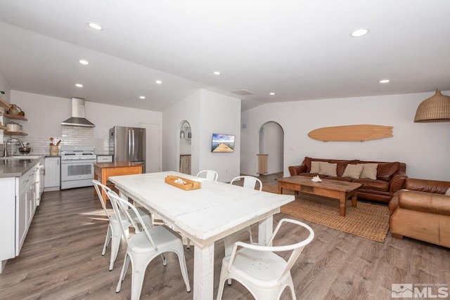 dining area featuring lofted ceiling, light wood-type flooring, arched walkways, and recessed lighting