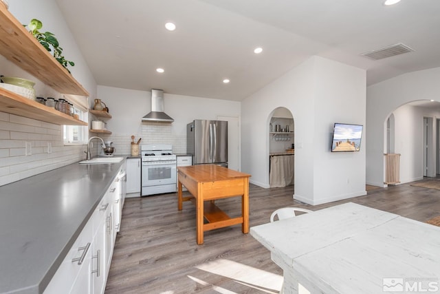 kitchen featuring white gas range, visible vents, freestanding refrigerator, a sink, and wall chimney range hood