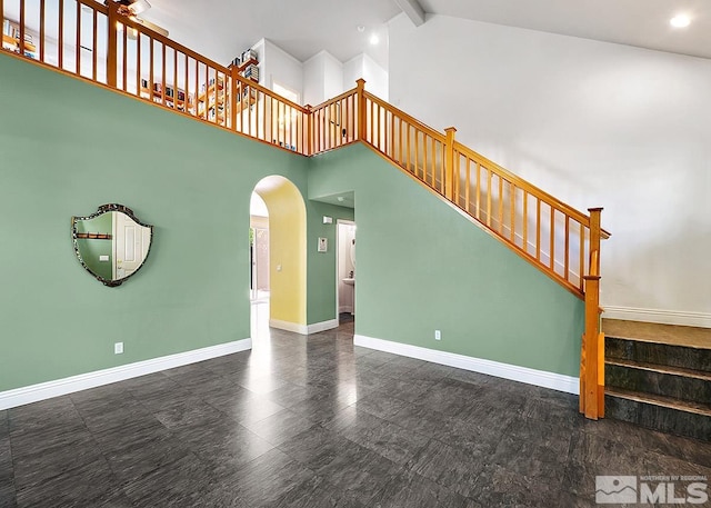 unfurnished living room featuring baseboards, arched walkways, beamed ceiling, stairs, and high vaulted ceiling