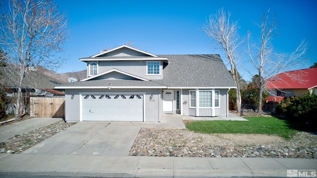 traditional-style home featuring roof with shingles, a front yard, fence, a garage, and driveway