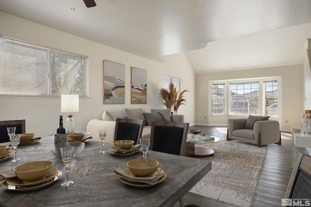 dining space featuring a fireplace, lofted ceiling, ceiling fan, wood finished floors, and baseboards