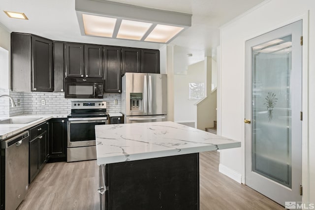 kitchen featuring a center island, stainless steel appliances, light wood-style floors, a sink, and dark cabinets