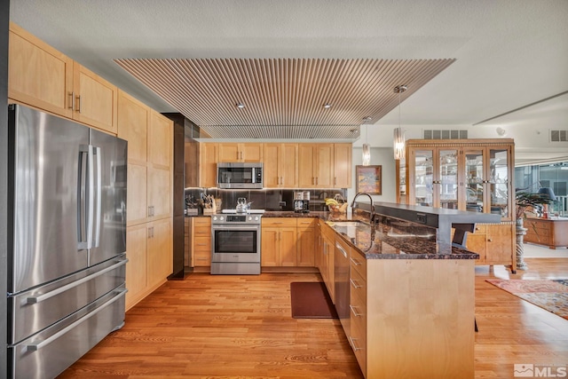 kitchen with light brown cabinets, stainless steel appliances, a peninsula, a sink, and visible vents