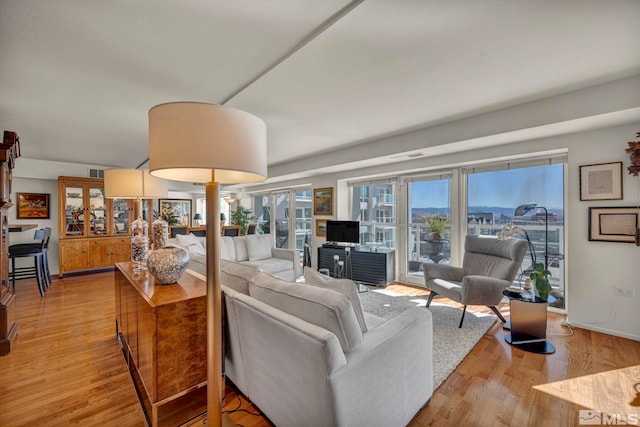 living room with light wood-style floors, visible vents, and baseboards