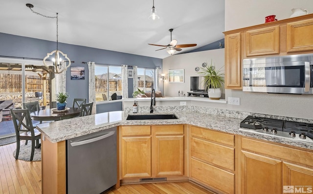 kitchen featuring lofted ceiling, light wood-style flooring, a sink, appliances with stainless steel finishes, and light stone countertops