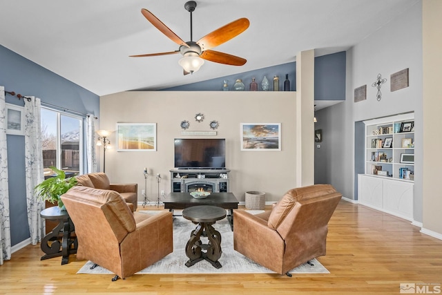 living area featuring ceiling fan, wood finished floors, high vaulted ceiling, a lit fireplace, and baseboards