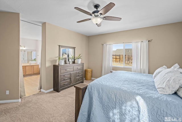 bedroom with a ceiling fan, light colored carpet, ensuite bath, and baseboards