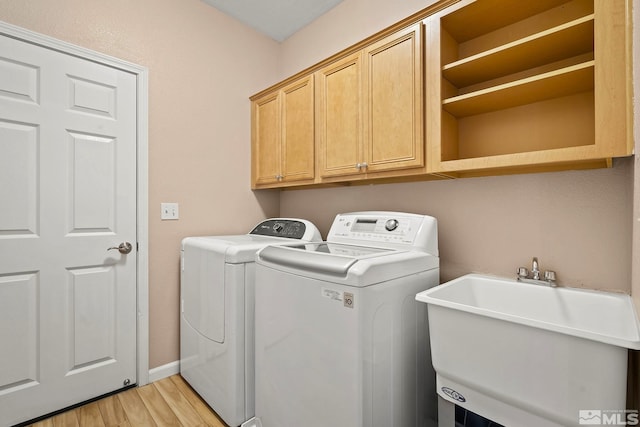 clothes washing area with cabinet space, baseboards, washing machine and clothes dryer, light wood-type flooring, and a sink