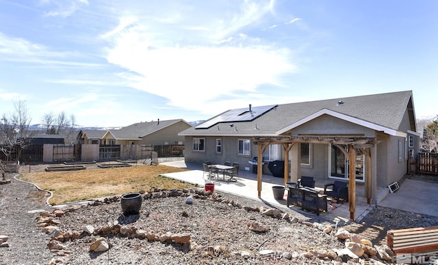 rear view of house with a patio, a fenced backyard, roof with shingles, roof mounted solar panels, and a pergola