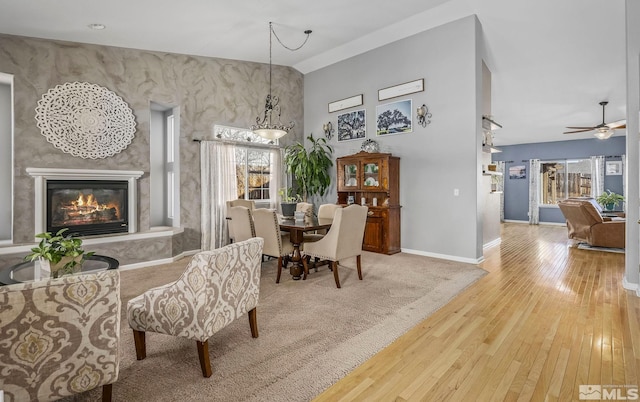 dining room featuring wood-type flooring, a high ceiling, a ceiling fan, a large fireplace, and baseboards