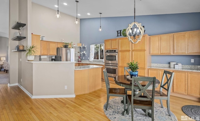 kitchen with light wood-style flooring, appliances with stainless steel finishes, a high ceiling, light brown cabinetry, and pendant lighting