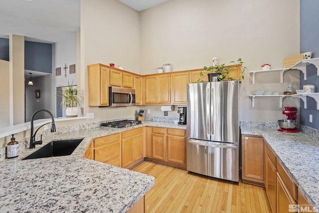 kitchen with light stone counters, a sink, a towering ceiling, appliances with stainless steel finishes, and light wood finished floors