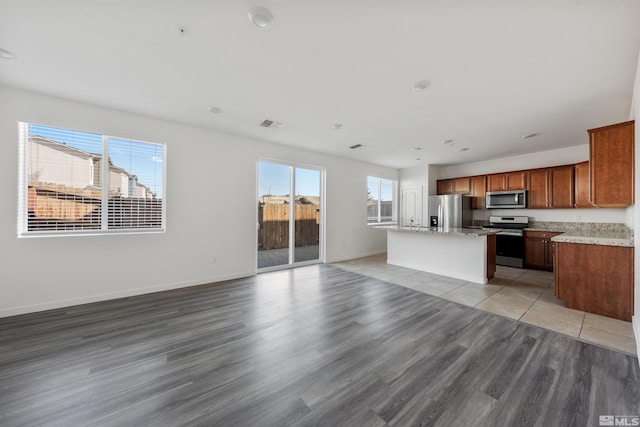 kitchen featuring a kitchen island, open floor plan, appliances with stainless steel finishes, light wood-type flooring, and brown cabinets