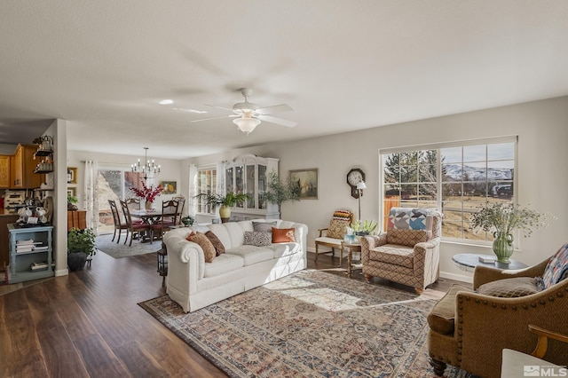 living room featuring dark wood-style floors, plenty of natural light, baseboards, and ceiling fan with notable chandelier