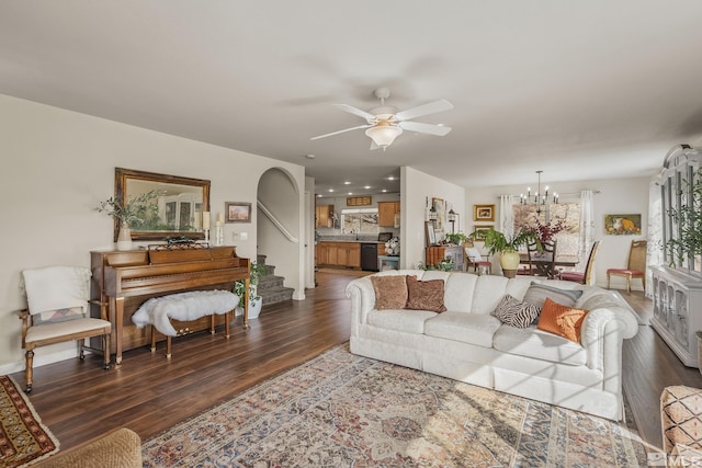 living area featuring stairway, arched walkways, dark wood-style flooring, and ceiling fan with notable chandelier