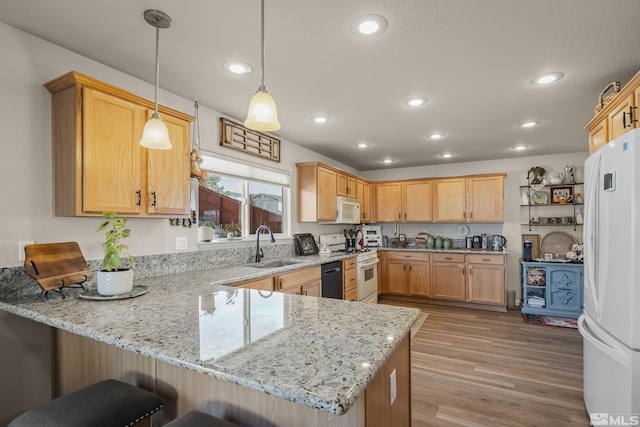 kitchen featuring light stone counters, a breakfast bar area, a sink, white appliances, and a peninsula