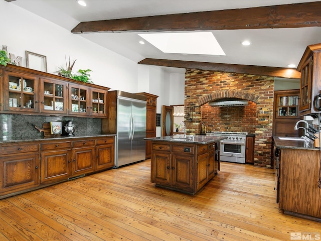 kitchen featuring high end appliances, light wood-type flooring, a sink, and decorative backsplash