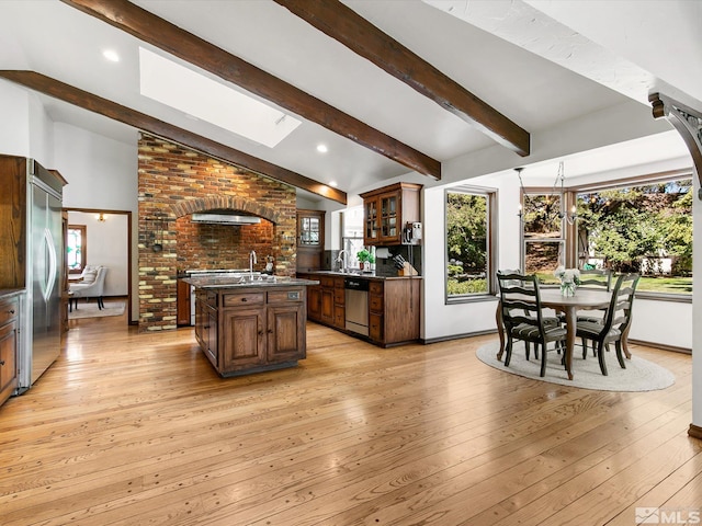 kitchen featuring appliances with stainless steel finishes, dark countertops, light wood-style floors, and vaulted ceiling with skylight