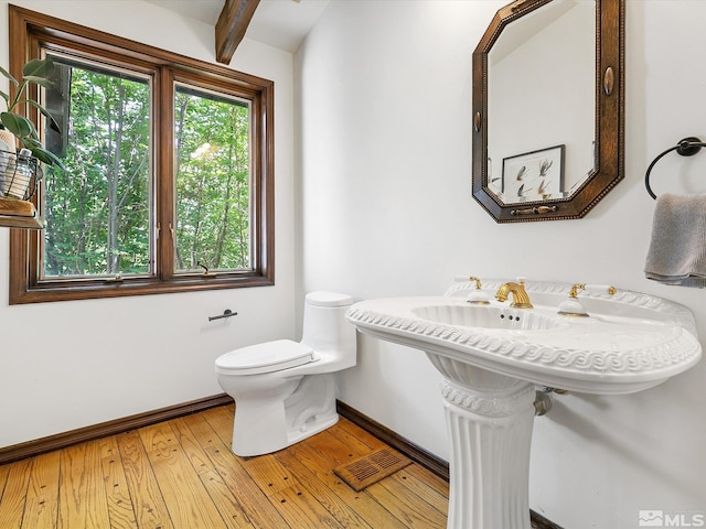 half bathroom with visible vents, baseboards, toilet, wood-type flooring, and beam ceiling